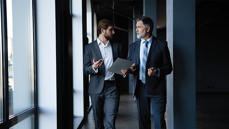 Two colleagues communicating in a modern office corridor.